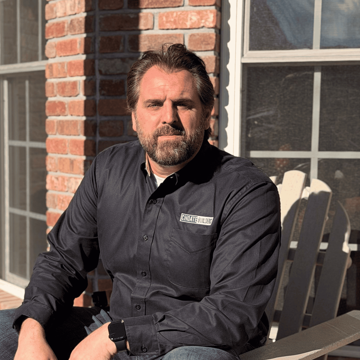 Construction Professional Construction professional sitting outdoors in front of a brick building, wearing a black shirt with.